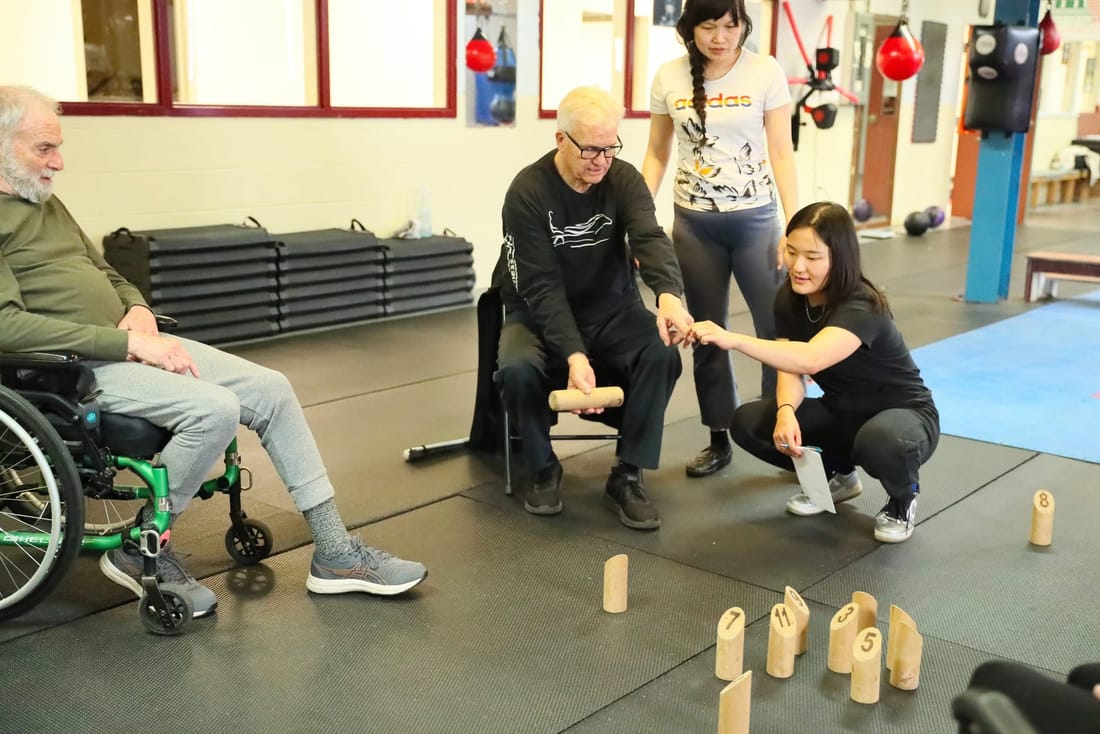 Participants, one seated in a wheelchair, playing a throwing game together during an SCI PEI activity session